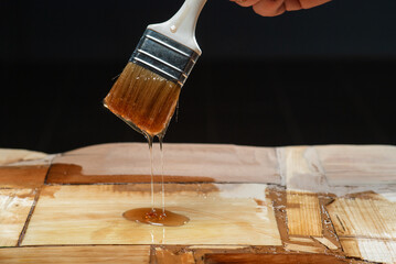Hand holding a brush applying varnish paint on a wooden surface