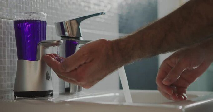 Man standing on a stool to reach the sink is diligently washing his hands with soap and water in a clean bathroom.