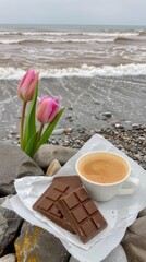 Pink tulips in a flowerpot sit next to a cup of coffee on the beach