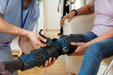 A male nurse helps to put a bondage, medical splint, knee brace on the leg of an elderly female patient who communicates with the attending physician at the clinic or hospital.