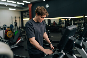 Portrait of athletic man in activewear adjusting settings on treadmill, preparing for cardio...