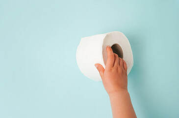 Roll of white toilet paper in child hand. blue background with copy space