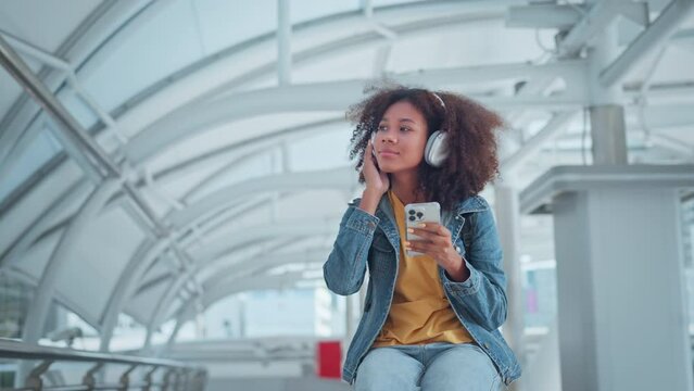 Attractive young African American woman putting headphones and enjoying dancing music on the urban city, Female listening to music, song, podcast, or audiobook.