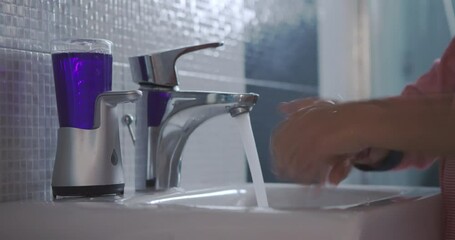A young boy standing on a stool to reach the sink is diligently washing his hands with soap and water in a clean bathroom.