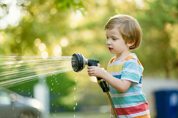 Cute little boy playing with garden hose on hot summer day. Child playing with water at summertime. - 794964601