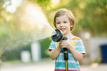 Cute little boy playing with garden hose on hot summer day. Child playing with water at summertime. - 794964816