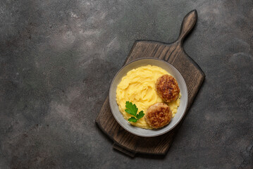 Mashed potatoes with meat cutlet in a bowl on a wooden board, dark grunge background. Top view, flat lay, copy space.