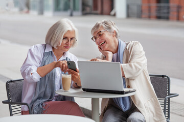 Elderly businesswomen at business meeting in outdoor cafe in the city. Beautiful mature senior women with gray hair discuss business matters with a laptop at the table