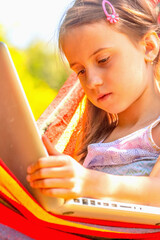 Portrait of young beautiful girl relaxing in hammock while working on laptop. She learning and communicates online remotely.  Vertical image.