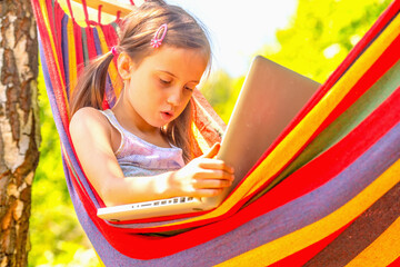 Portrait of young beautiful girl relaxing in hammock while working on laptop. She learning and communicates online remotely.