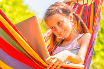 Young girl relaxing in hammock while working on laptop. She learning and communicates online remotely. Horizontal image.