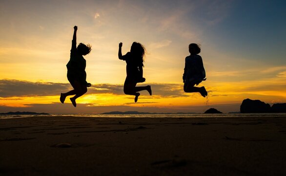 Silhouettes of three people jumping joyfully on the beach at sunset, conveying a sense of freedom and celebration, suitable for summer or travel-related themes.