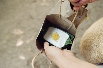 An eco-friendly takeout container with yellow accents is held within a paper bag, suggesting...