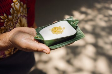 A hand presenting a Thai dessert made with tapioca pearls on banana leaf, indicative of Thai...