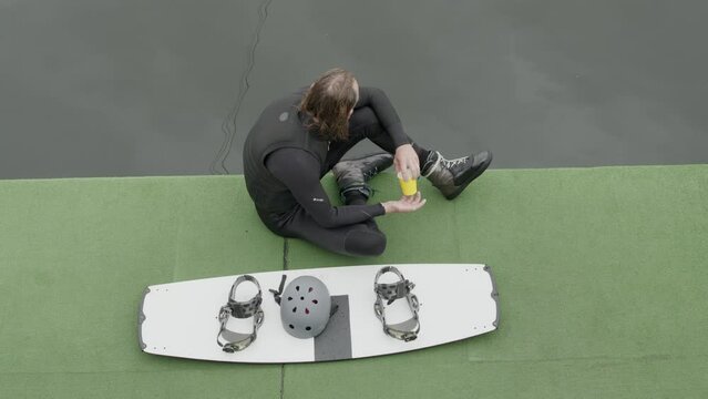 Top view shot of adult male wakeboarder sitting on dock and looking at water while resting after wakeboarding training at cable park