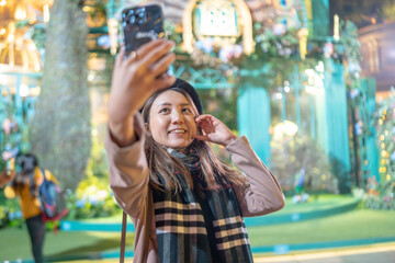 A young Hong Kong woman in her 20s taking a selfie in front of a monument in a shopping center in...