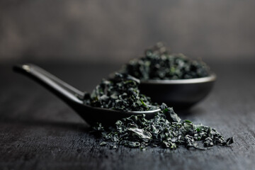 Dried wakame seaweed in spoon on black table.