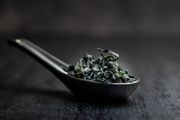 Dried wakame seaweed in spoon on black table. - 794993863