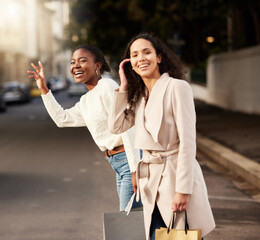 Women, city and calling for taxi after shopping with smile, happiness with sale on product. Female friends, together and hand sign with fashion in urban for car, transport or travel from sidewalk
