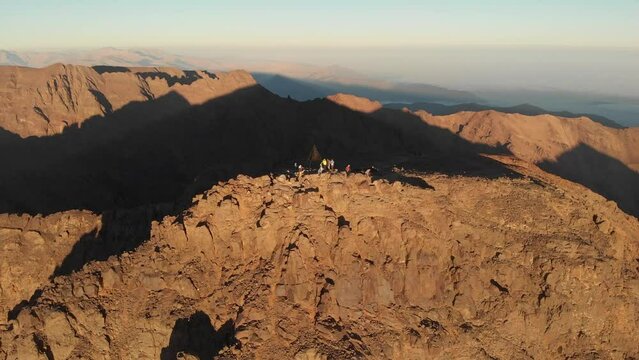 Toubkal, Morocco - A group of young travlers of summit of Mount Toubkal in the Atlas Mountains (Aerial drone view in 4K) - CIRCA 2021