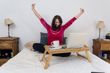 Entertained adult woman watching movies on laptop happy with arms open held sitting on bed