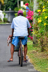 Blue Bay, Grand Port district, Mauritius, Africa - man carrying caught fishes in hand while riding a bike