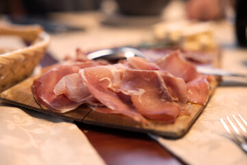 vista in primo piano su un'antipasto a base di prosciutto crudo servito su un tagliere di legno e con sfondo sfuocato