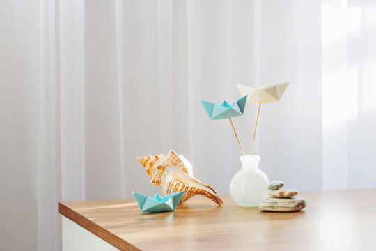 paper boats in glass vase with sea decor on wooden table