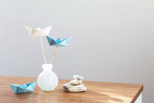 paper boats in glass vase with sea stones  on wooden table