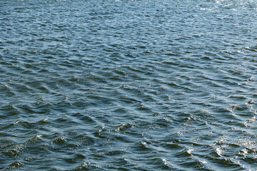 visuale in primo piano, leggermente dall'alto, di una superficie acquatica color azzurro di un fiume, increspata da piccole onde, di giorno