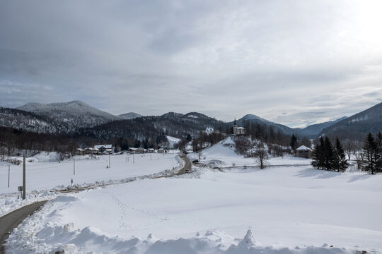 ampia visuale panoramica del piccolo paese di Lokve, in Slovenia, circondato da montagne, colline e vasti boschi completamente innevati, sotto un cielo coperto e grigio, in inverno
