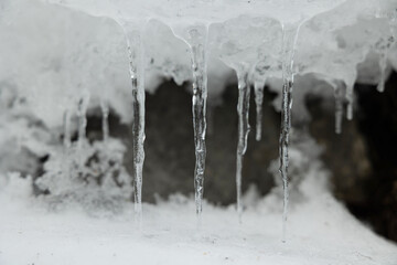 visuale in primo piano e di fronte di varie stalattiti di ghiaccio in un ambiente naturale di montagna, che si sono formate dallo scioglimento della neve sovrastante