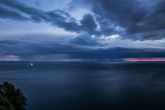 inquadratura panoramica dall'alto, vicino a Sistiana che mostra un temporale lontano che si abbatte sul Golfo di Trieste, nel Mare Adriatico, di sera, al tramonto, con un cielo completamente nuvoloso,