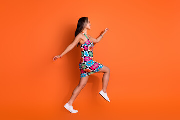Full length photo of good mood cute girl dressed print clothes run on summer sale to empty space isolated on orange color background