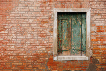 Fototapeta na wymiar The facade of a typical exposed brick house with window and green shutters in Venice, Italy