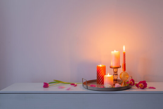 pink tulips   and burning candles  on tray on background wall