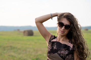 a beautiful girl with curly hair rests on a field next to a haystack on a warm and sunny summer day	
