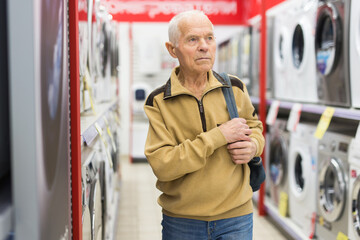 Elderly man choosing washing machine in showroom of electrical appliance store - 795083239