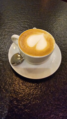 A cortado in a coffee cup, with a spoon, on a saucer cappuccino