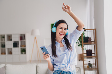 Photo of nice lady dance listen music headphones smart phone wear blue shirt bright interior flat indoors