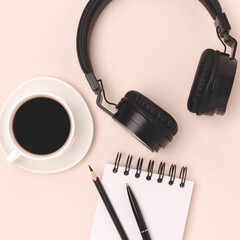 Cup of black coffee, headphones, notepad and stationery on a beige background. Minimal concept.