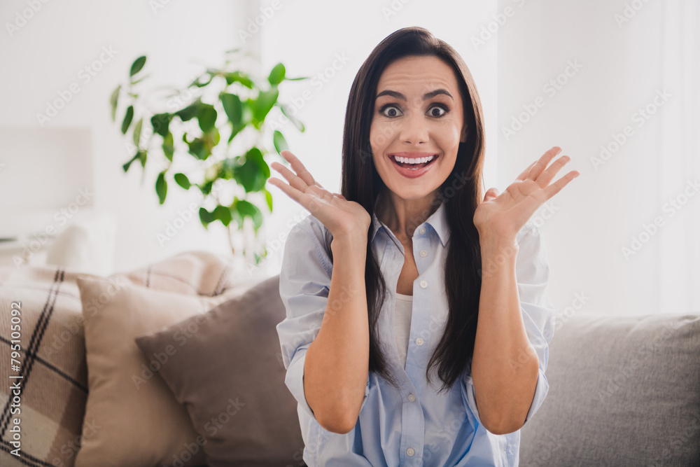 Poster Photo of excited funky lady dressed blue shirt sitting couch smiling rising hands arms indoors house room