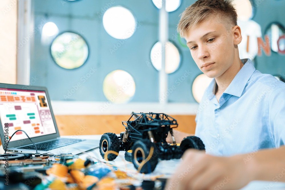Poster schoolboy watching and considering parts of robotics car while learning technology in stem class. on