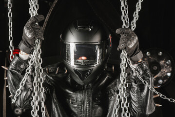 Brutal motorcyclist rider in black helmet and black studded leather jacket on a dark background.