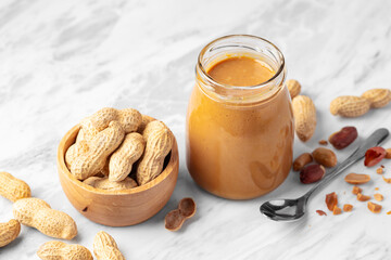 Peanut butter in jar and peanuts in wooden bowl on kitchen marble table