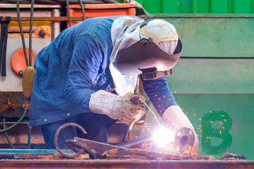 Welder with safety equipment is welding steel pipe in outdoors workshop for use to improving oil pipeline systems work in tanker ship