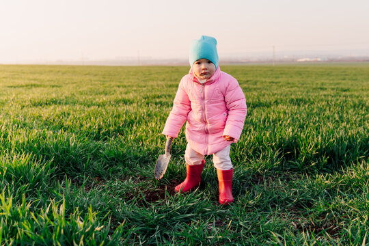 Portrait of child little girl in the field with a shovel