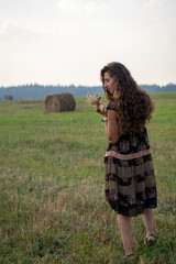 Naklejka na ściany i meble a beautiful girl with curly hair rests on a field next to a haystack on a warm and sunny summer day 