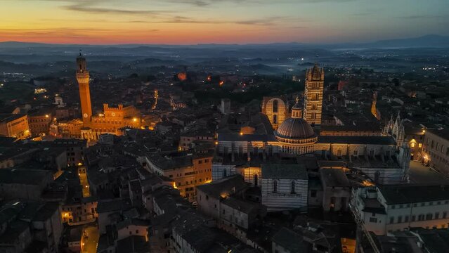 Siena, Tuscany, Italy - aerial view of medieval town at sunrise. Flying over Torre del Mangia and Duomo di Siena with city lights. HDR 4K shot