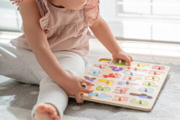 Close up image of a little girl playing with a wooden alphabet letter puzzle. Montessori methodology and materials, education, development and learning in the childhood stage - obrazy, fototapety, plakaty